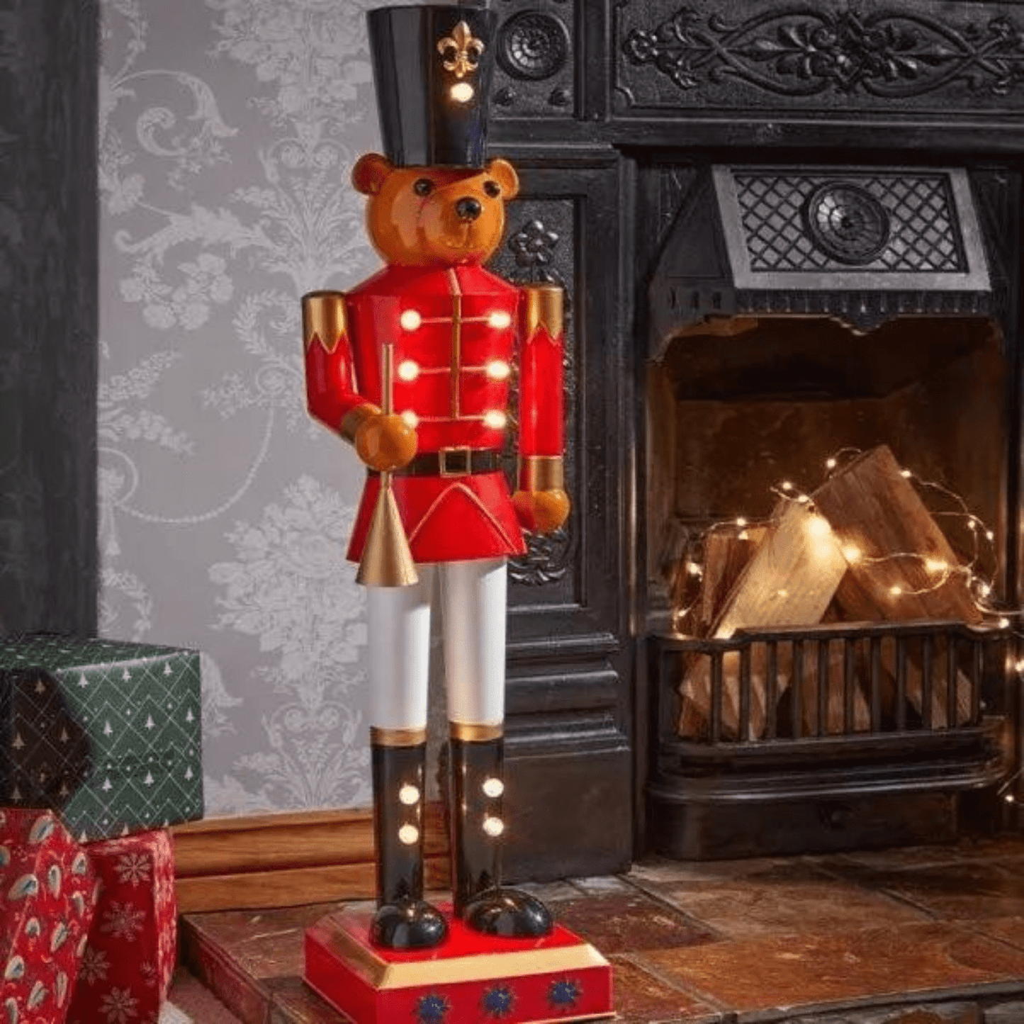 Decorative teddy bear Nutcracker figure in front of a fireplace with Christmas presents.