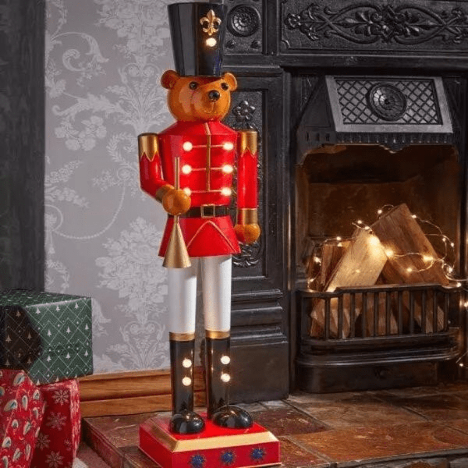 Decorative teddy bear Nutcracker figure in front of a fireplace with Christmas presents.