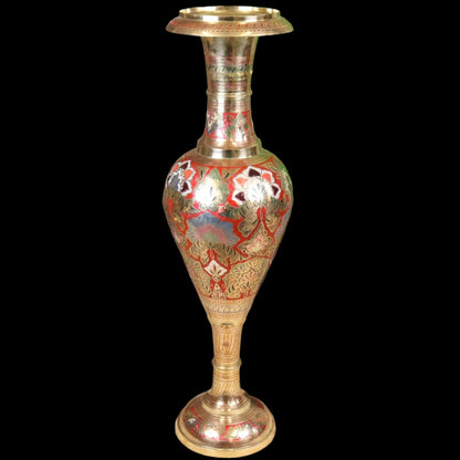 Decorative vase with floral patterns on a wooden floor with a plant and wooden cabinet in the background.