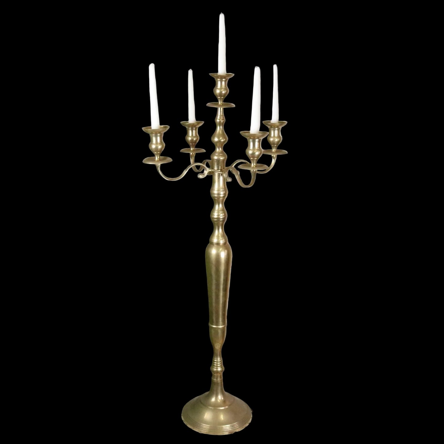 Brass candelabra with candles on a decorative stand against a rustic brick wall.