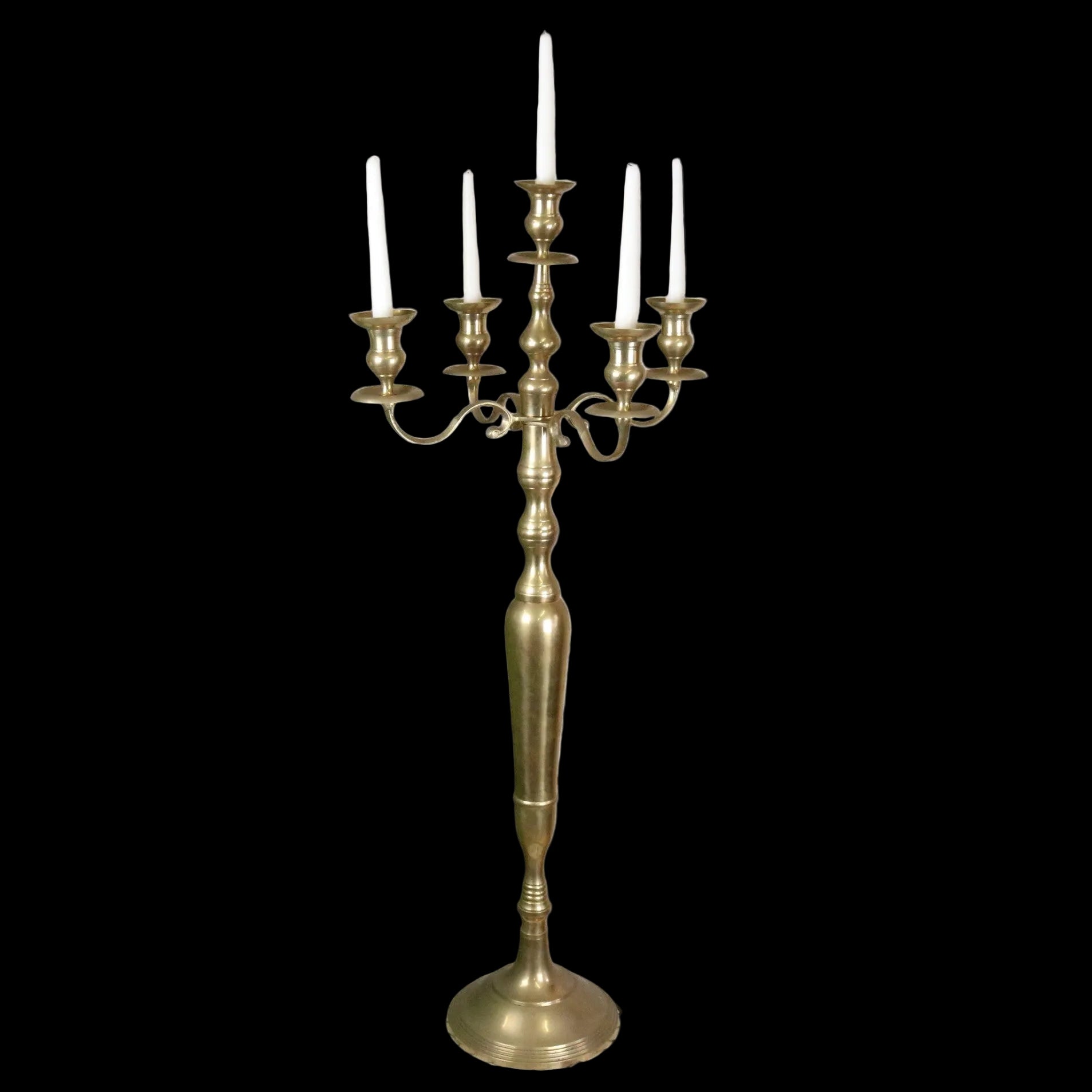 Brass candelabra with candles on a decorative stand against a rustic brick wall.