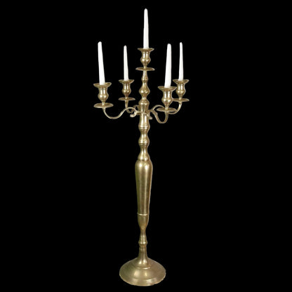 Brass candelabra with candles on a decorative stand against a rustic brick wall.