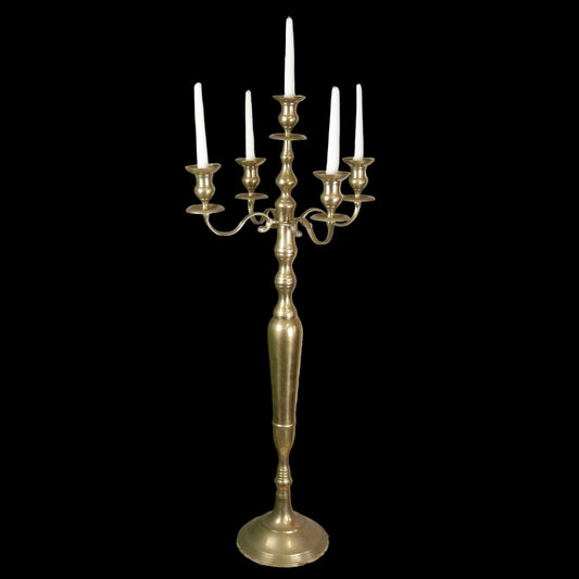 Brass candelabra with candles on a decorative stand against a rustic brick wall.