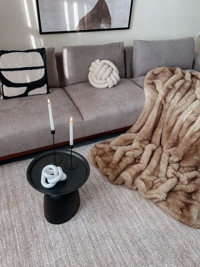 Living room with a gray sofa, decorative pillows, a beige throw blanket, and a small black table with candles.