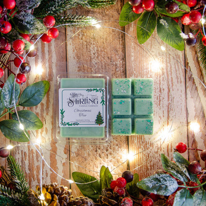 Green wax melts in a clear container with 'Sterling' branding, surrounded by Christmas decorations on a wooden background.